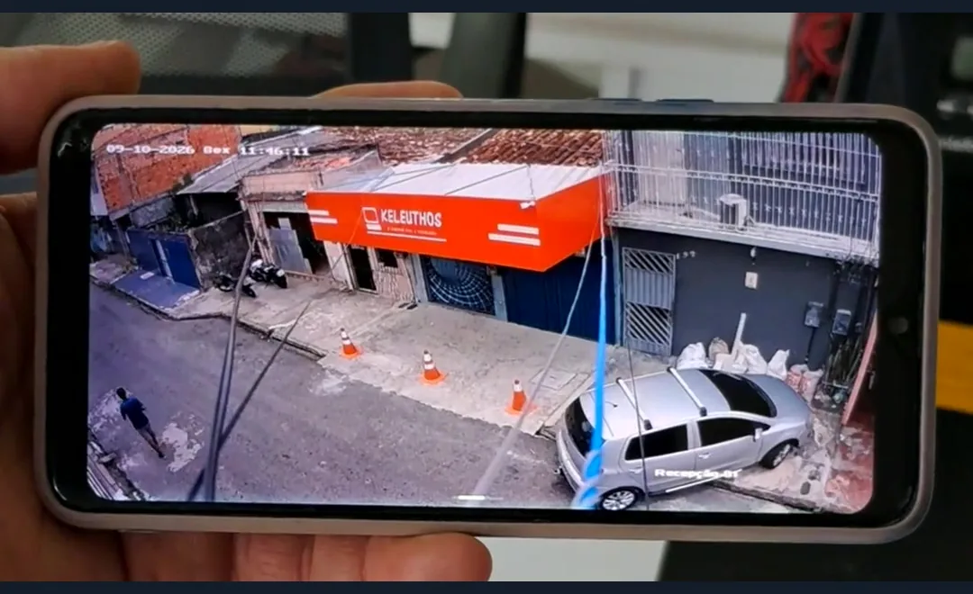 Celular exibindo ao vivo a imagem da câmera nova da fachada da Keleuthos, com a rua e um carro estacionado